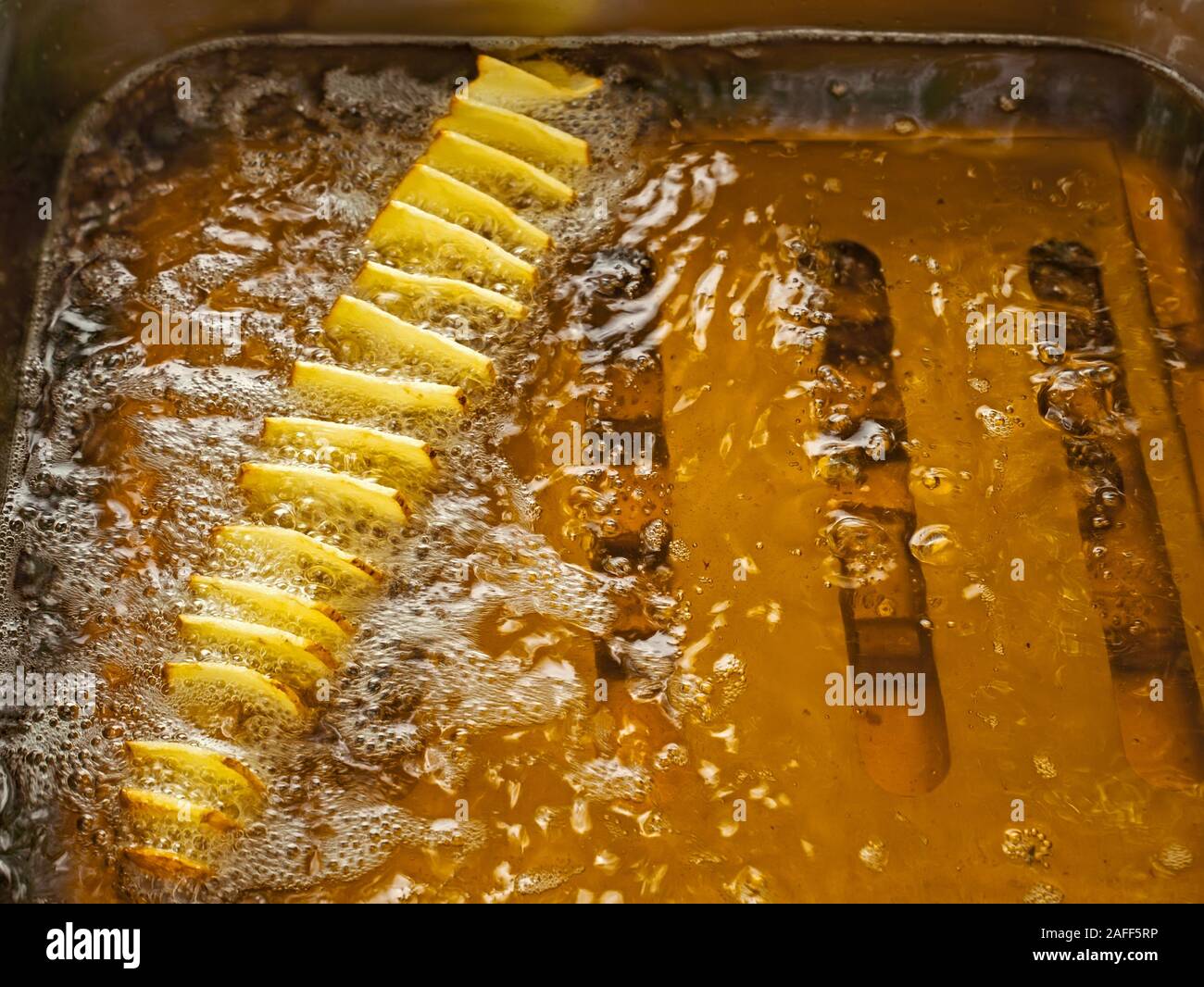 Thinly sliced potato slices are fried in metal tank, oil boiling in