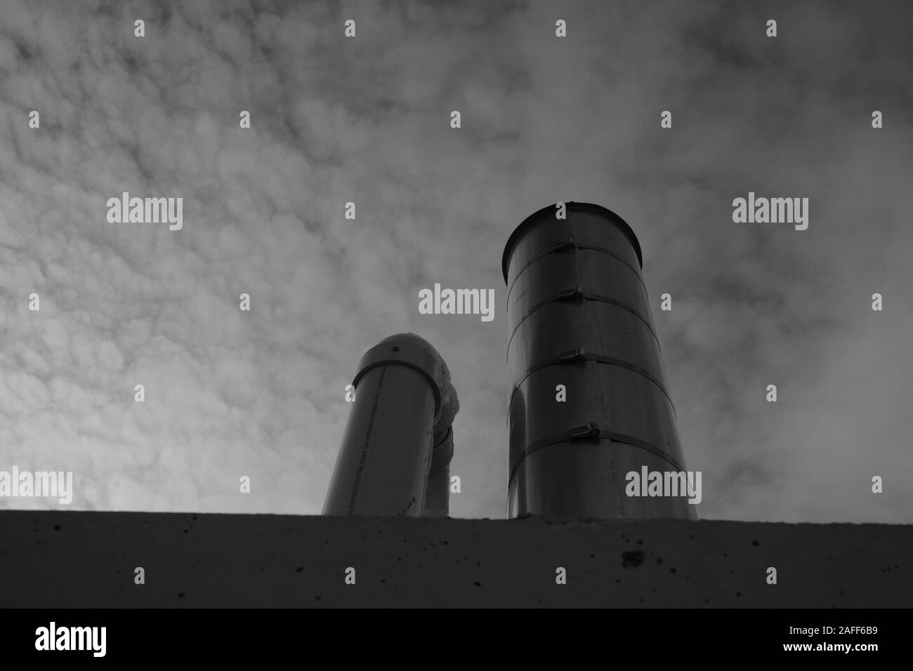 Black and white image of steel exhaust / heat exchange chimneys on the top of a garage, against a cloudy sky. Ottawa, Ontario, Canada. Stock Photo