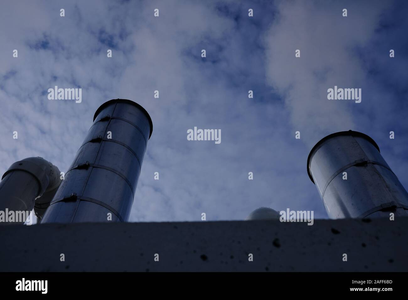 Steel exhaust / heat exchange chimneys on the top of a garage, against a cloudy blue sky. Ottawa, Ontario, Canada. Stock Photo