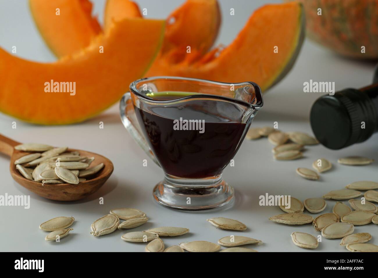 Pumpkin oil in a gravy boat and in a bottle against a white background