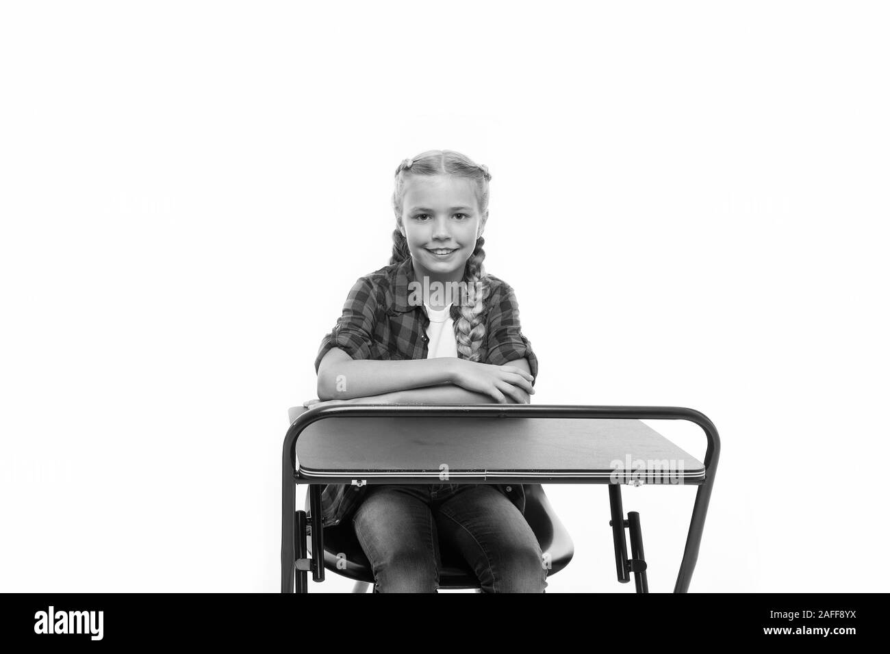 Back to school. Cute school child sitting at desk isolated on white. Little schoolgirl having lesson in primary school. Adorable small girl enjoying her school time. Stock Photo