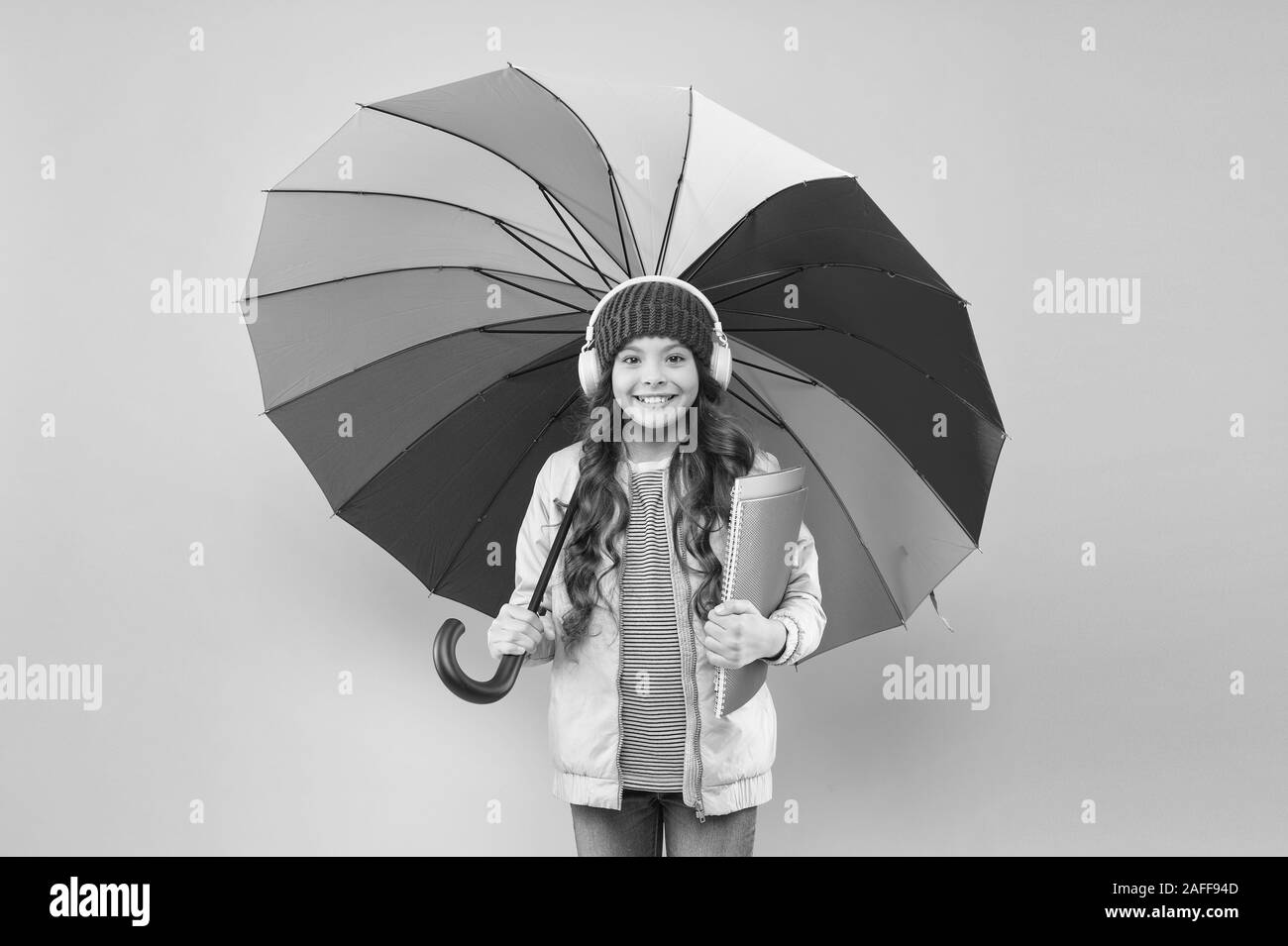 Designed for rainy weather. Little school girl hold colorful umbrella on pink background. Small child back to school in autumn. Adorable kid in earphones go to school on rainy day. The best school. Stock Photo