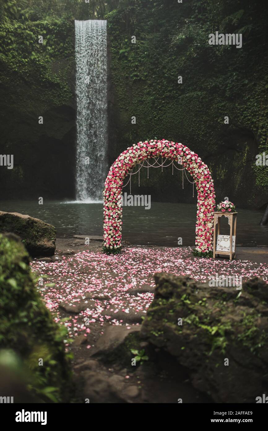 Wedding ceremony on small secret waterfall Tibumana in Bali, Indonesia jungle. Classic round arch with pink and white roses. Unusual destination for wedding. Stock Photo