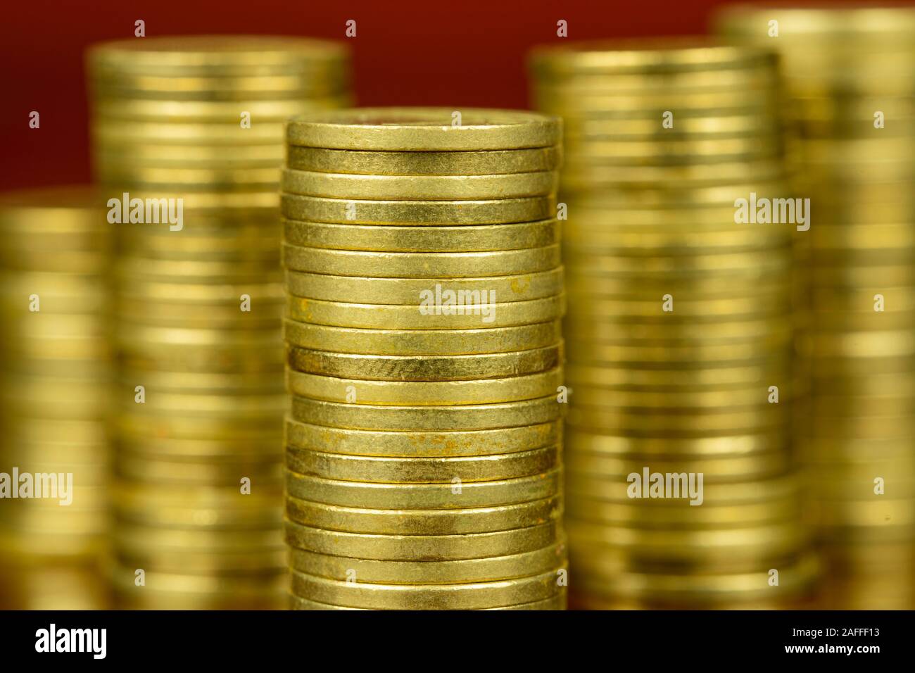 Shiny stack of golden coins. Close up photo. Business concept. Reflection on the table. Red background. Stock Photo