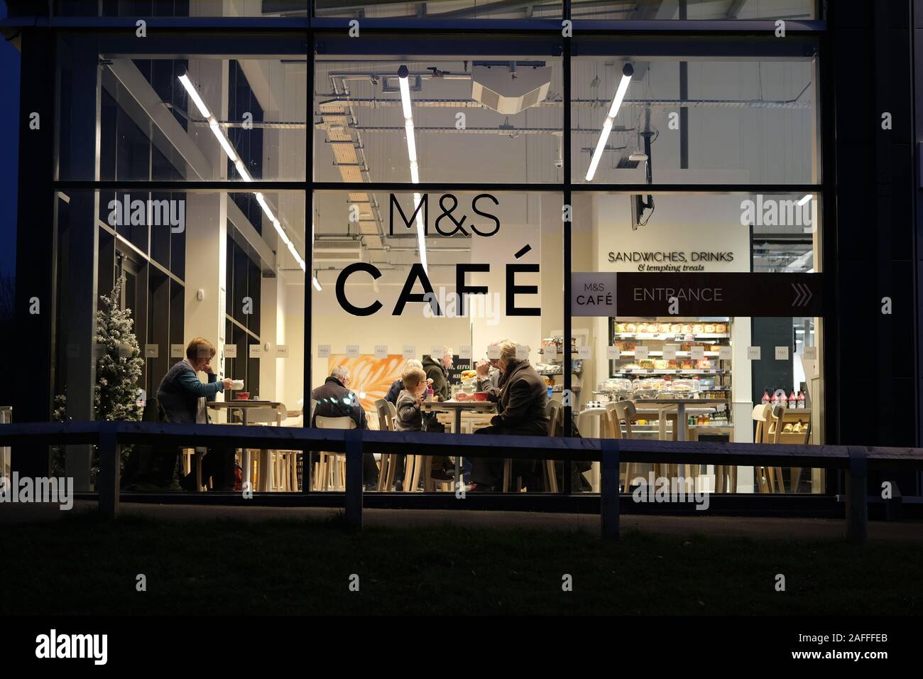 M&S Cafe with people enjoying their meals seen through the windows at night. Stock Photo