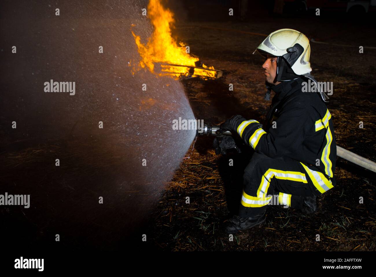 Group of firemen in protective suits putting out a fire with a water hose Stock Photo