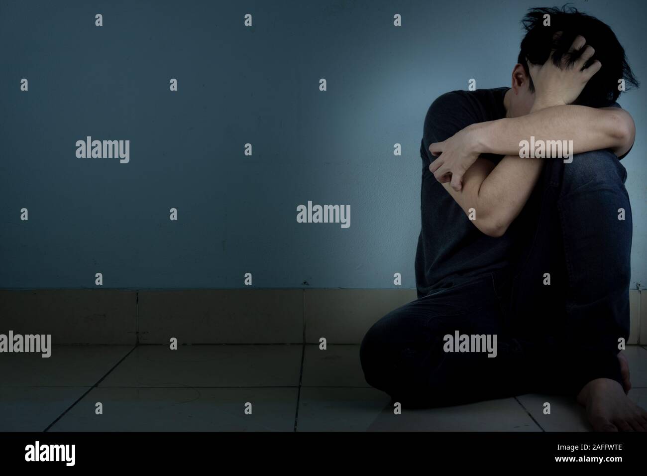 sad man hug his knee and cry sitting alone in a dark room. Depression ...