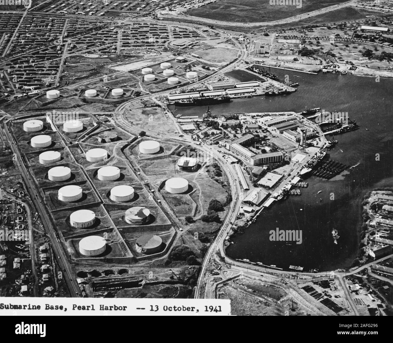Pearl Harbor - Aerial view of the Submarine Base (right center) with the fuel farm at left, looking south on 13 October 1941. Among the 16 fuel tanks in the lower group and ten tanks in the upper group are two that have been painted to resemble buildings (topmost tank in upper group, and rightmost tank in lower group). Other tanks appear to be painted to look like terrain features. Alongside the wharf in right center are USS Niagara (PG-52) with seven or eight PT boats alongside (nearest to camera), and USS Holland (AS-3) with seven submarines alongside. Before attack Stock Photo