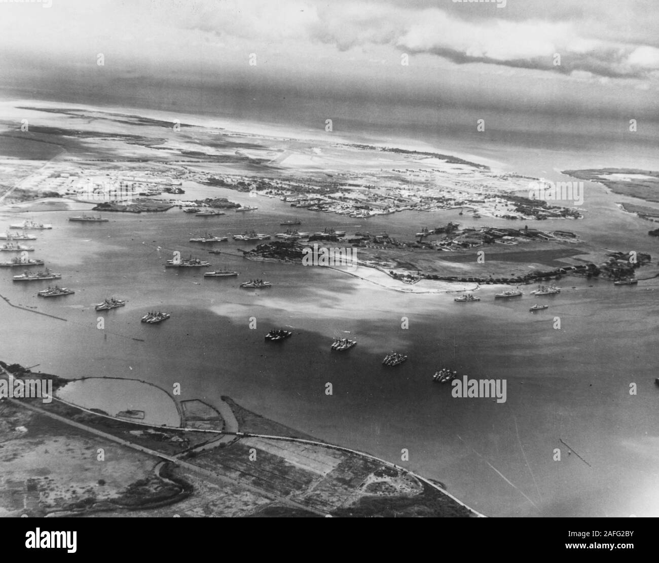 Pearl Harbor - Aerial photograph from 2500 feet altitude, looking southward, showing the U.S. Fleet moored in the harbor on 3 May 1940. This was soon after the conclusion of Fleet Problem XXI and four days before word was received that the Fleet was to be retained in Hawaiian waters. There are eight battleships and the carrier Yorktown (CV-5) tied up by Ford Island, in the center of the harbor. Two more battleships and many cruisers, destroyers and other Navy ships also present, most of them moored in groups in East Loch, in the foreground. A few of the destroyers are wearing experimental dark Stock Photo