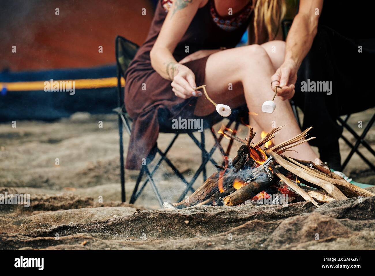 Cropped image of travelers using sticks when frying marshmallows on fire Stock Photo