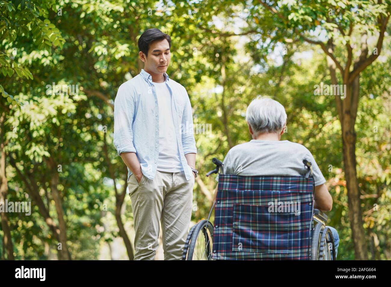 asian son talking to sad and depressed wheelchair bound father Stock Photo