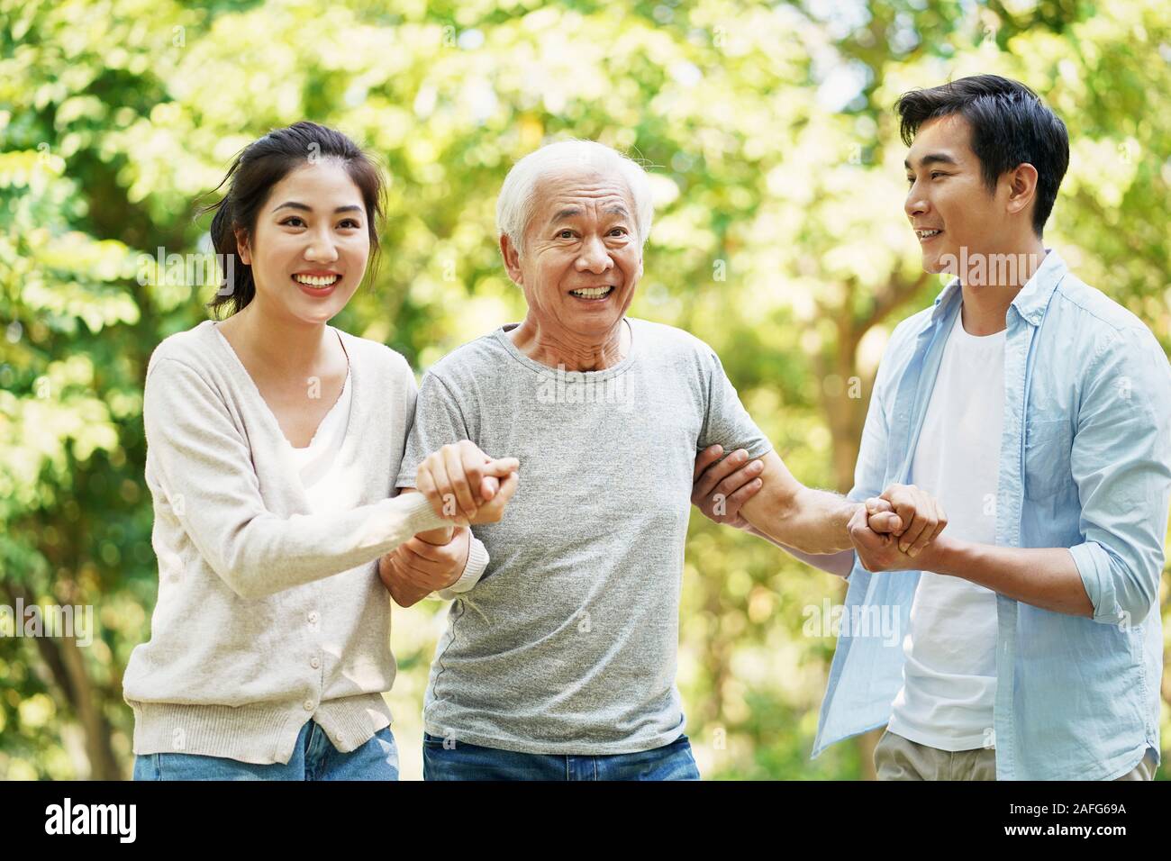 young asian couple helping father stand up and walk outdoors in park Stock Photo