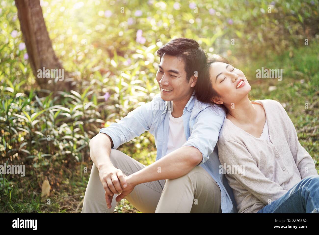 happy young asian couple sitting on ground talking daydreaming Stock Photo