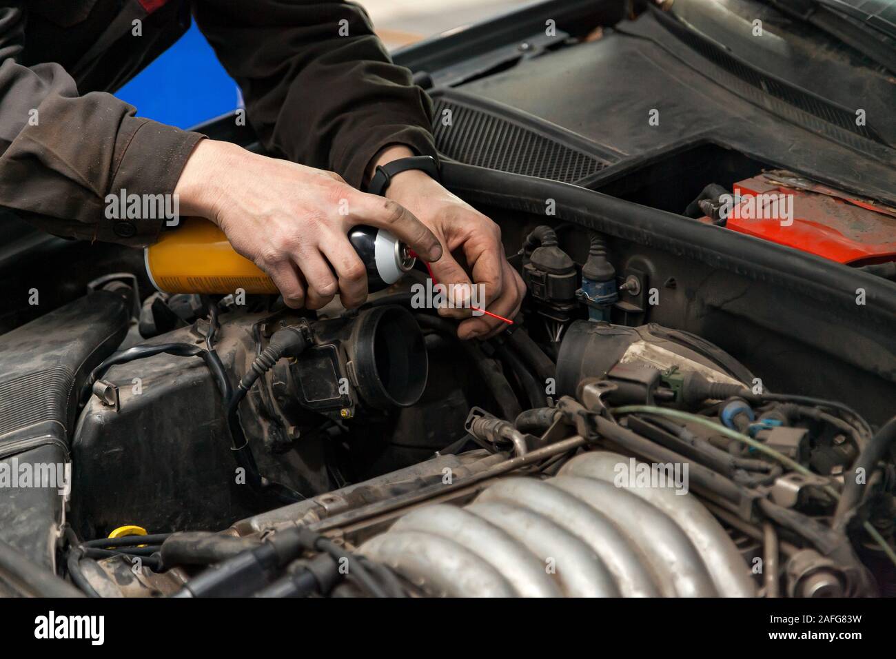 A male mechanic with a can spray gasoline into the intake manifold to