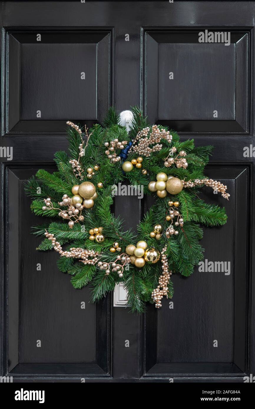 Gold and green christmas wreath on a black wooden house door. London, England Stock Photo