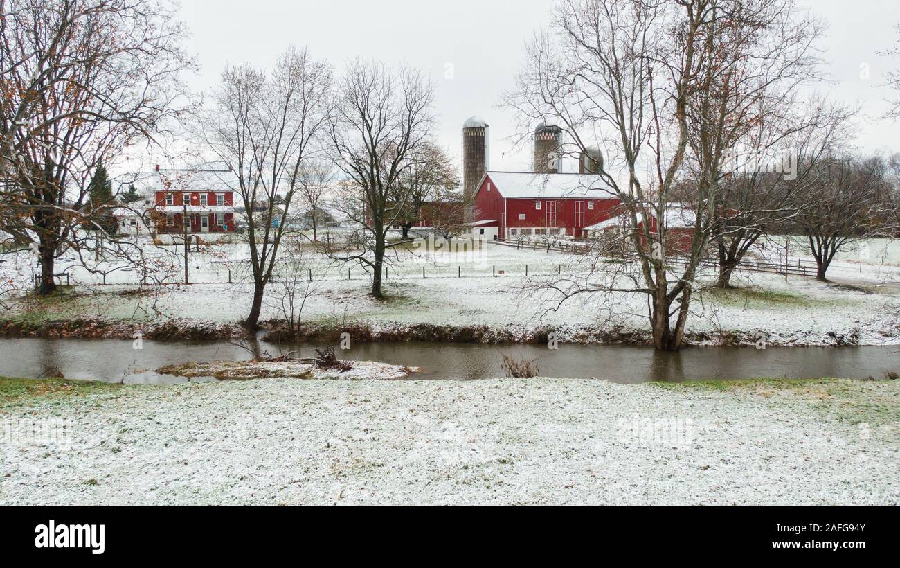 Aerial view of traditional farm in Pennsylvania, red buildings and barn, a small river in foreground, winterlandscape covered in snow Stock Photo