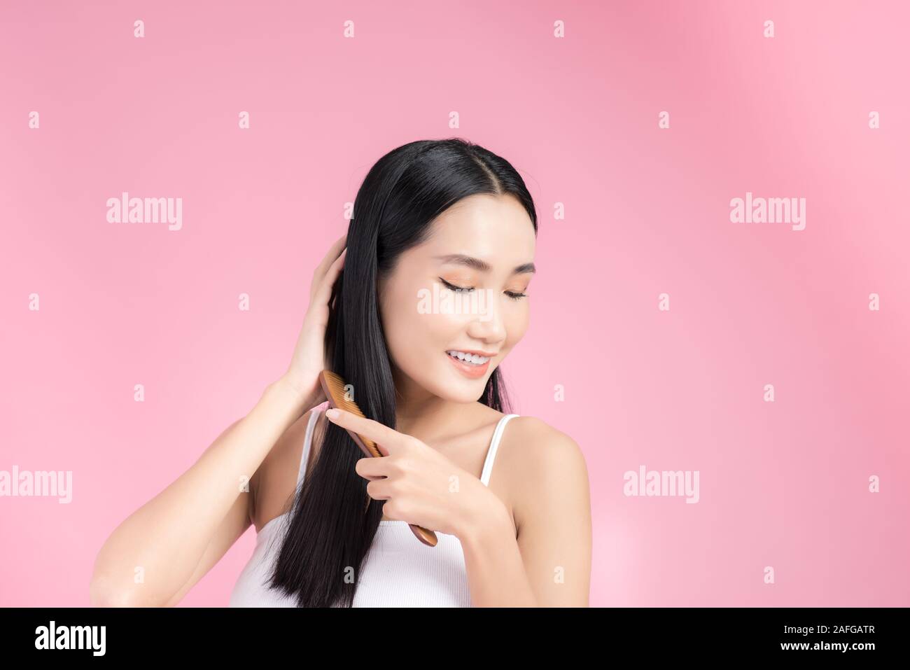 Happy Asian woman combing her beautiful black hair. Isolated on pink background. Stock Photo