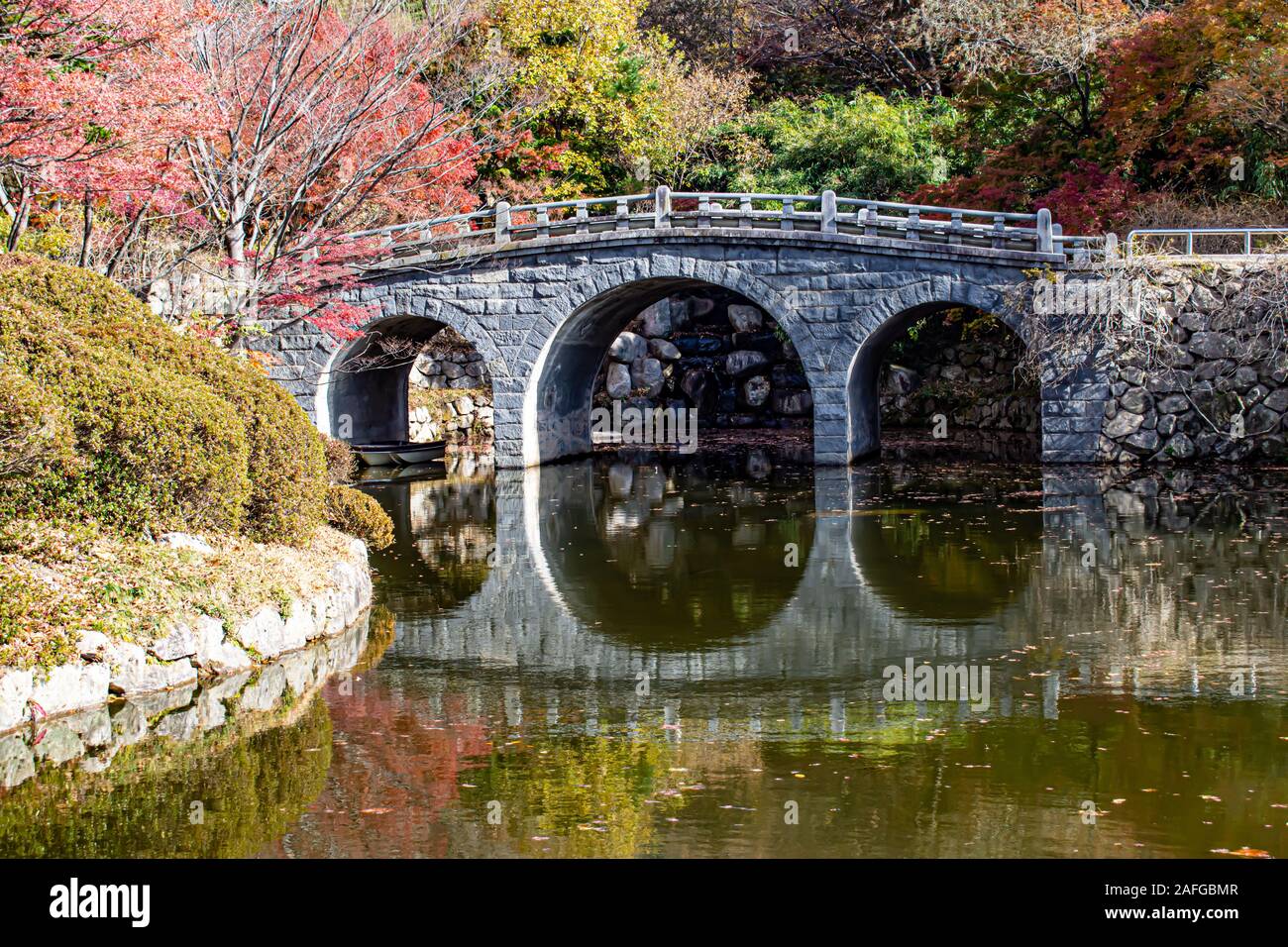 Ancient bridge in South Korean Mountains with a beautiful autumn display of colour reflecting in the lake. Stock Photo