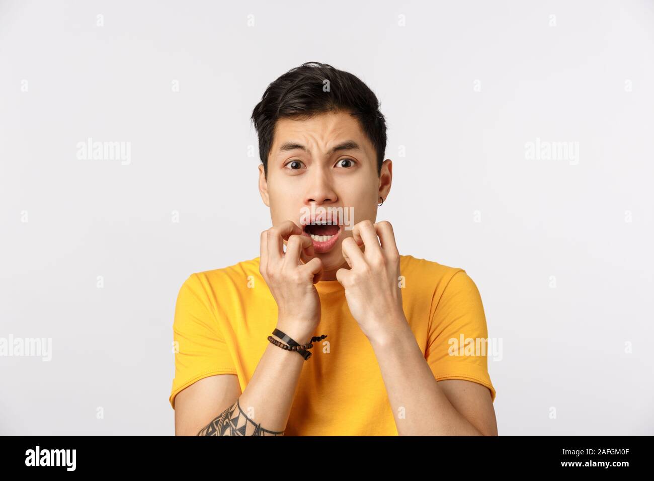 Close-up studio shot innocent young scared timid asian guy, hold hands over opened mouth, gasping and trembling fear, feeling like victim afraid hear Stock Photo