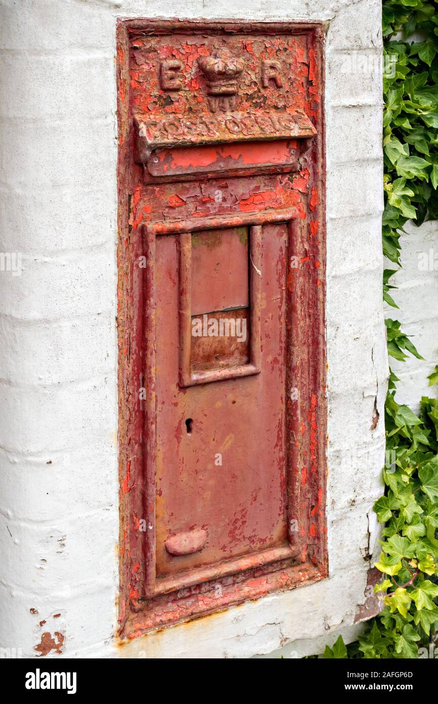 Distressed, old, disused, wall mounted, Royal Mail post box with peeling and faded red paint set into whitewashed wall, England, UK Stock Photo