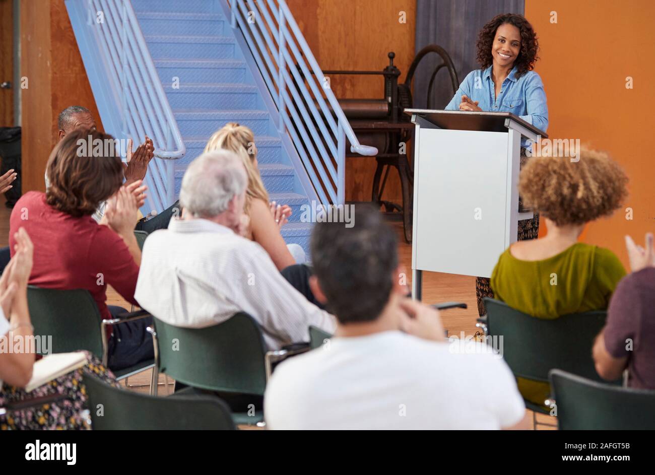 Woman At Podium Chairing Neighborhood Meeting In Community Centre Stock Photo