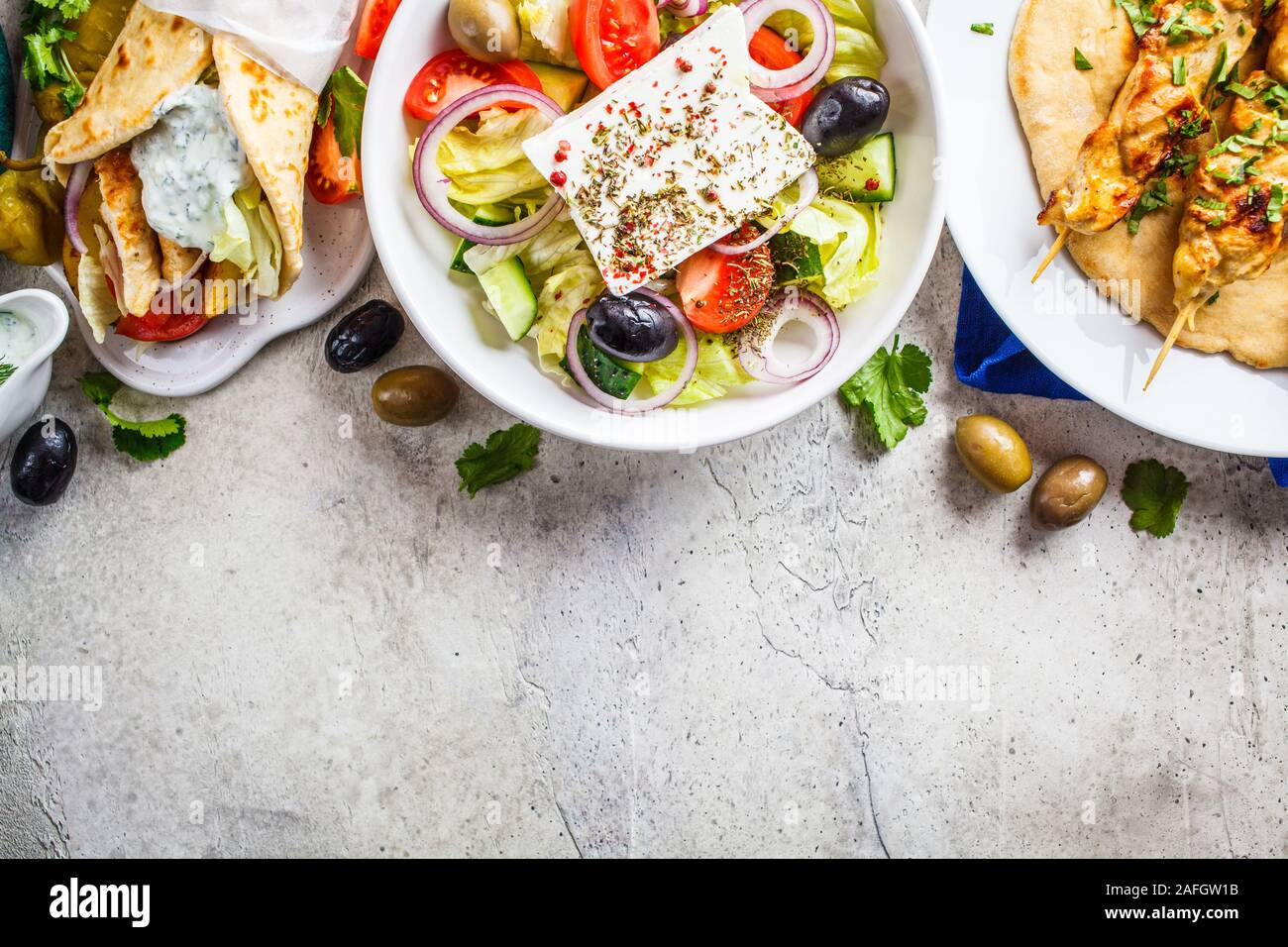 Greek food: greek salad, chicken souvlaki and gyro pita on gray background, top view. Traditional greek cuisine concept. Stock Photo