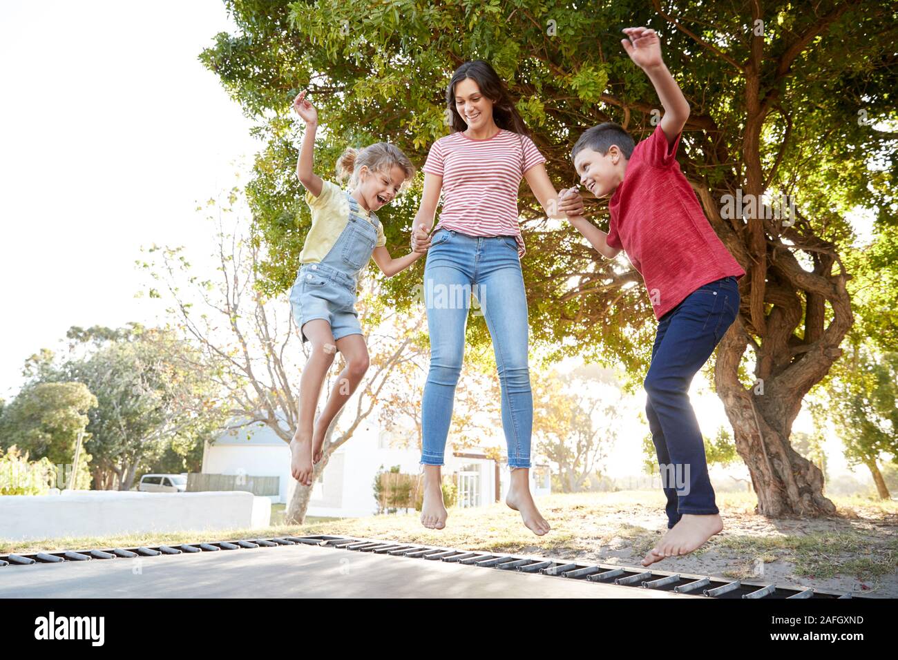 Siblings With Teenage Sister Playing On Outdoor Trampoline In Garden Stock Photo