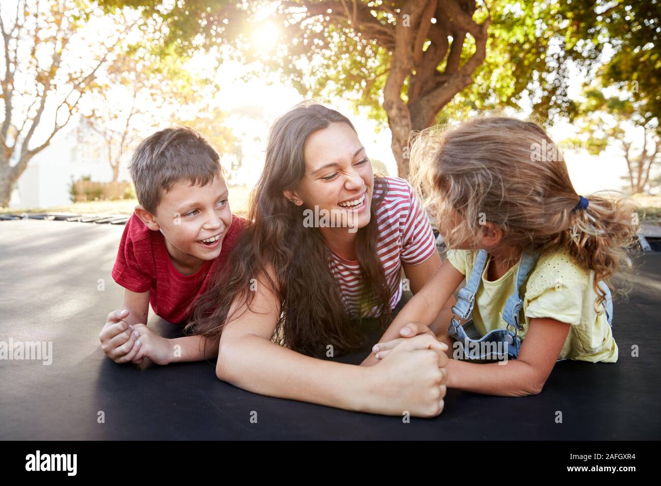 Siblings With Teenage Sister Playing On Outdoor Trampoline In Garden Stock Photo