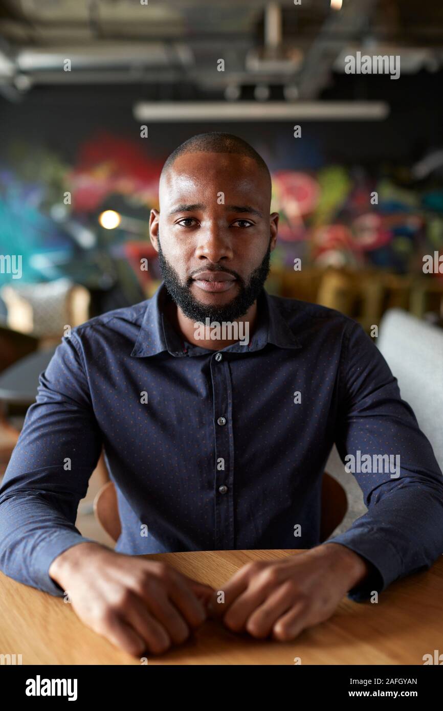 Mid adult black male creative sitting at a table in an office cafe looking to camera, close up Stock Photo