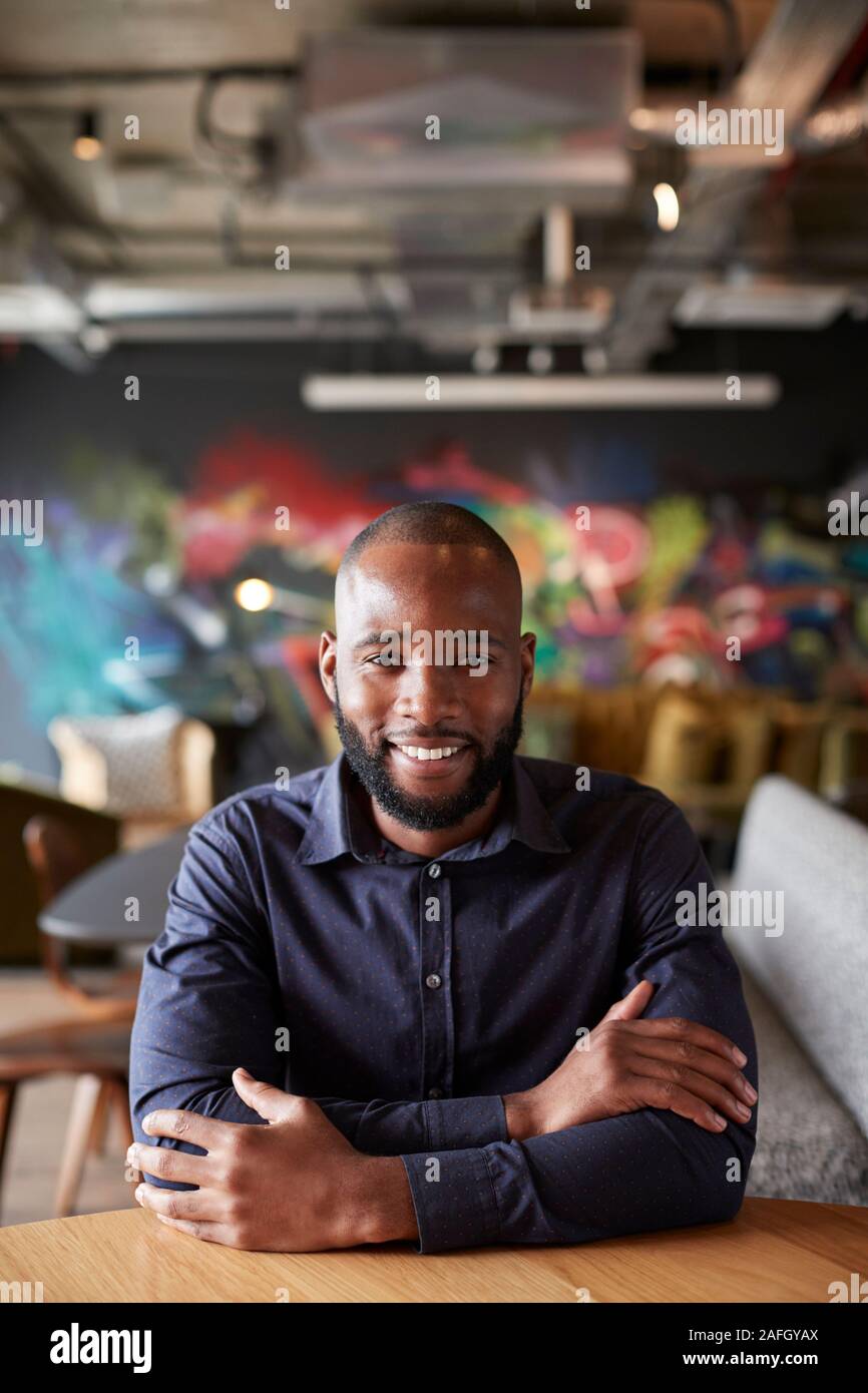 Mid adult black male creative sitting at a table with arms crossed smiling to camera, close up Stock Photo