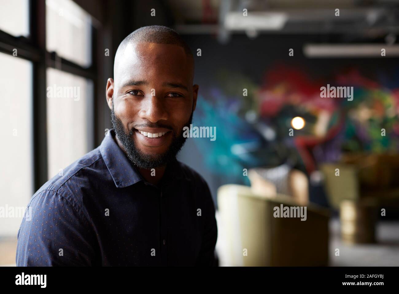 Mid adult black male creative in an office social area turning to camera smiling, close up Stock Photo