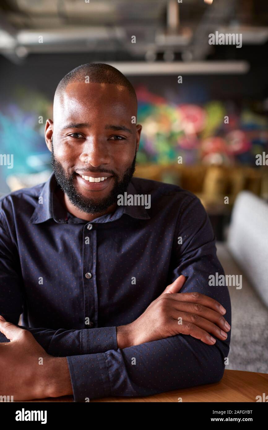 Mid adult black male creative sitting at a table in an office cafe smiling to camera, close up, crop Stock Photo
