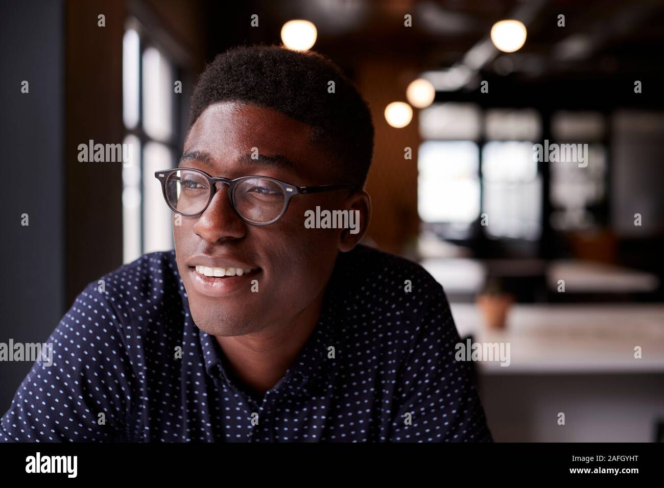 Young black male creative sitting at a desk in an office looking out of the window smiling, close up Stock Photo