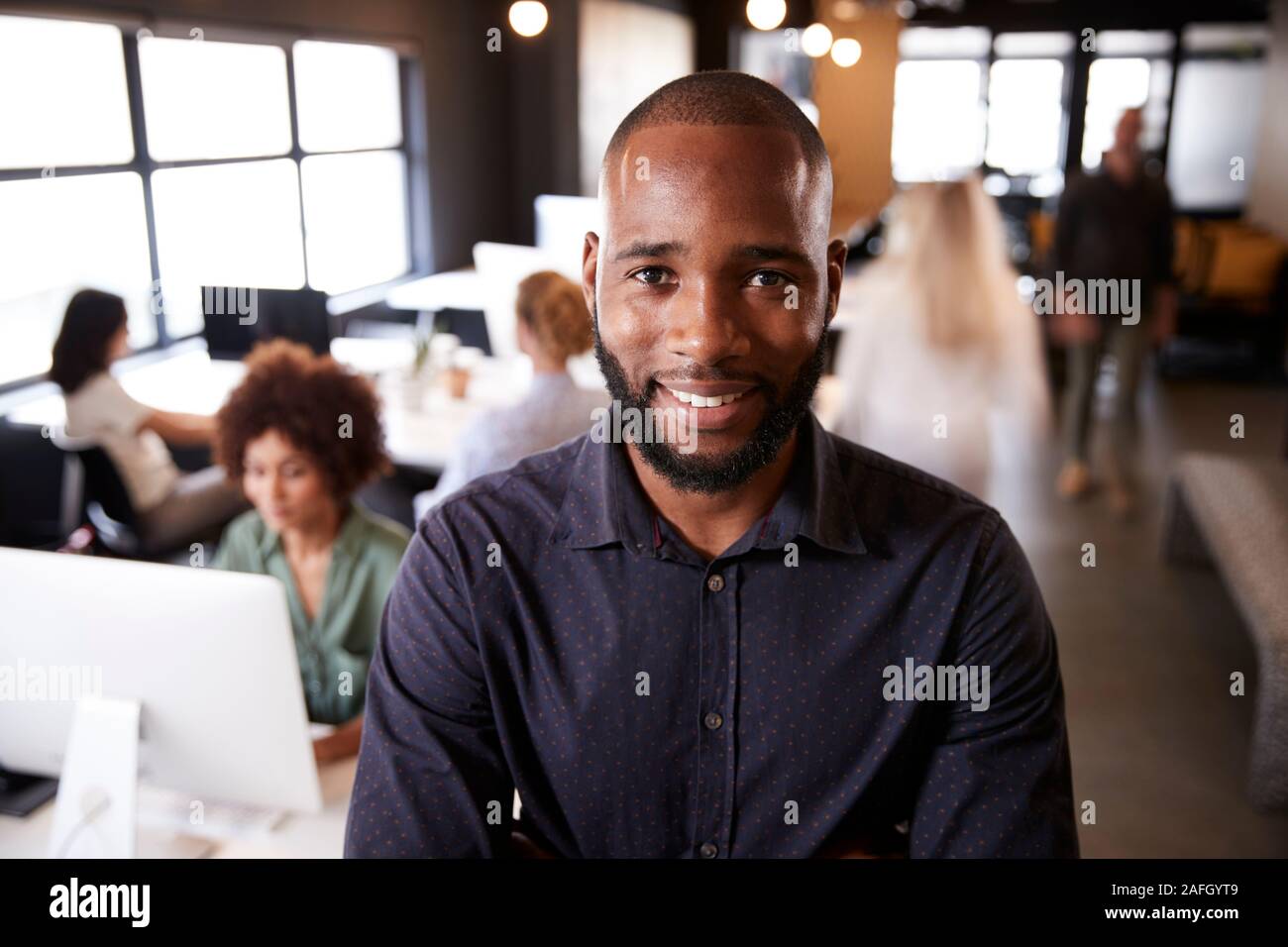 Bearded black male creative standing in a busy casual office, smiling to camera Stock Photo