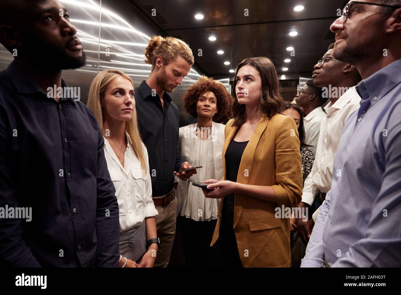 Work colleagues stand waiting together in an elevator at their office Stock Photo