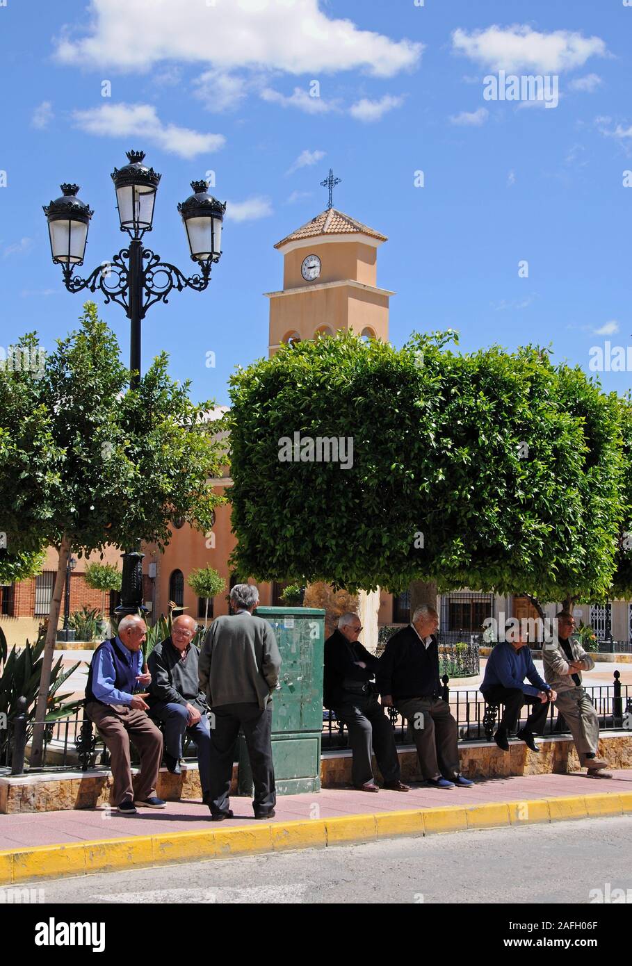 Elderly Spanish men chatting on the edge of the town square with the church tower to the rear, Albox, Almeria Province, Spain. Stock Photo