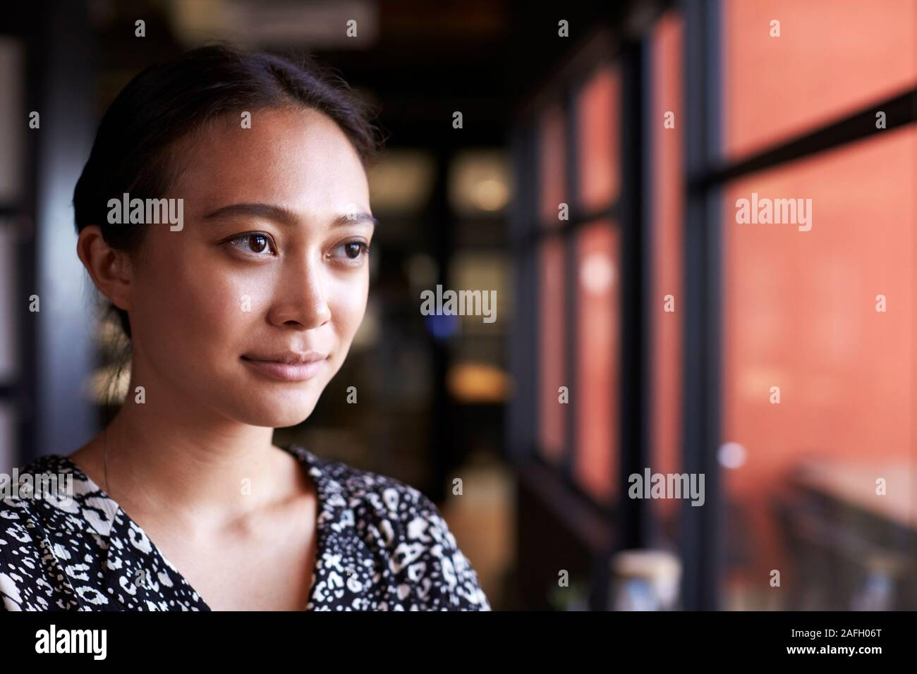 Millennial Asian businesswoman looking out of the window in an office, head and shoulders, close up Stock Photo