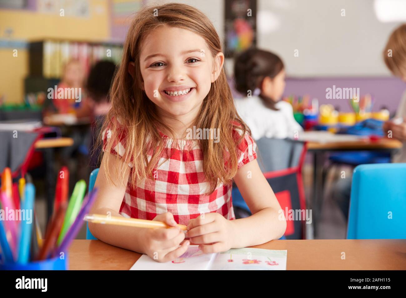 Portrait Of Smiling Female Elementary School Pupil Working At Desk Stock Photo