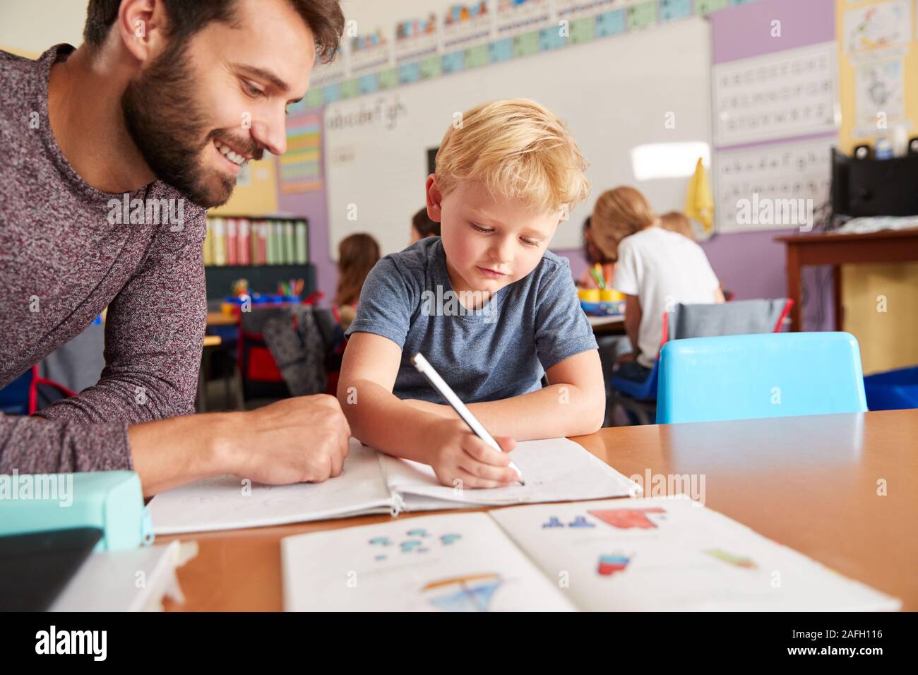 Elementary School Teacher Giving Male Pupil One To One Support In Classroom Stock Photo