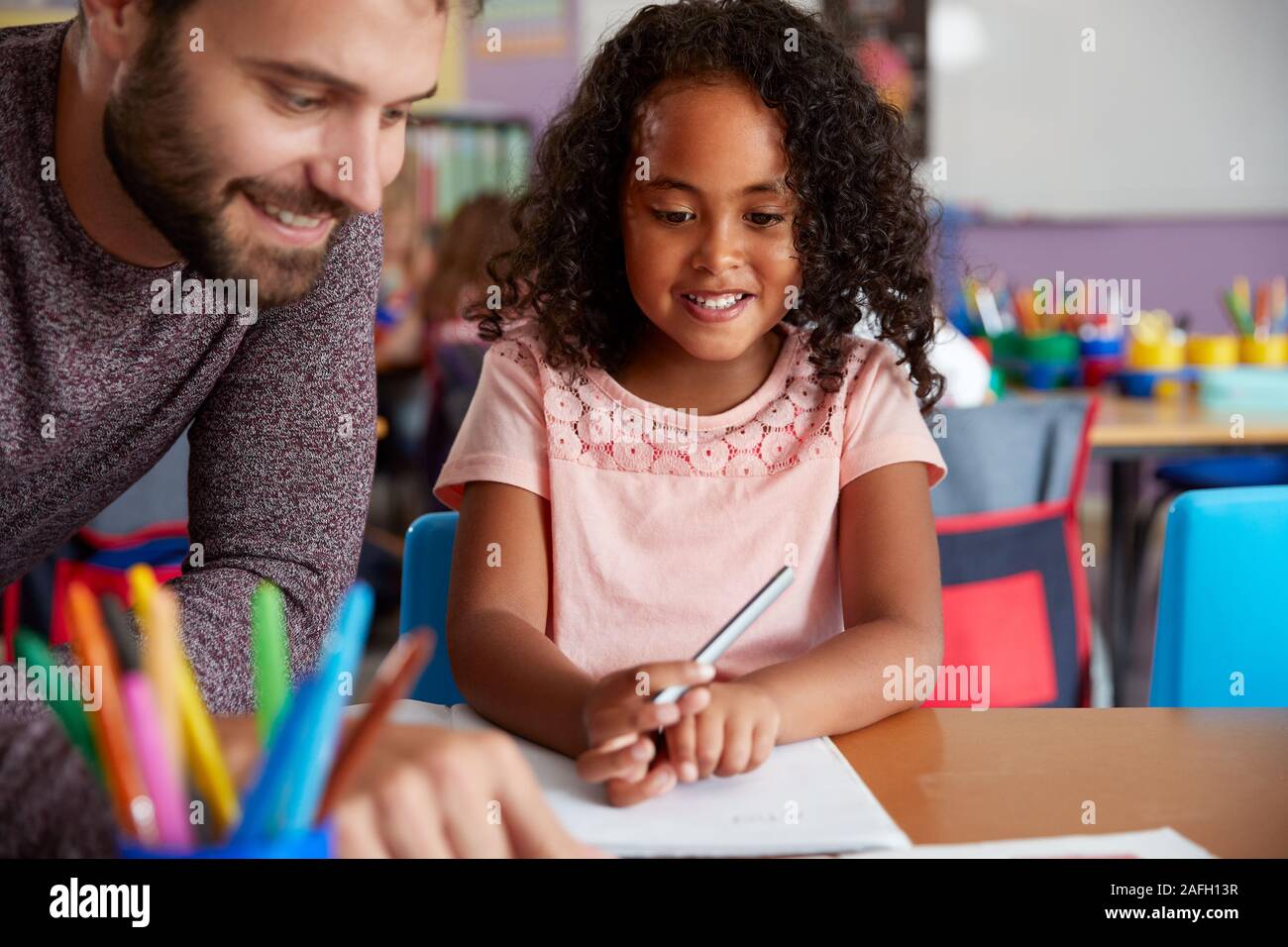 Elementary School Teacher Giving Female Pupil One To One Support In Classroom Stock Photo