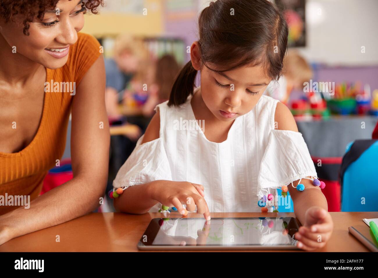 Elementary School Teacher And Female Pupil Drawing Using Digital Tablet In Classroom Stock Photo