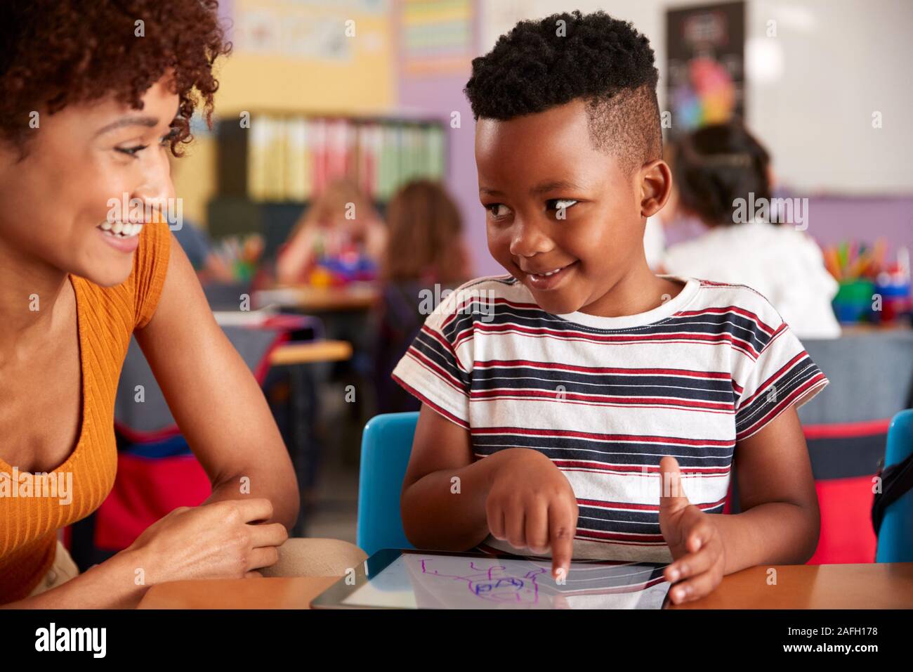 Elementary School Teacher And Male Pupil Drawing Using Digital Tablet In Classroom Stock Photo
