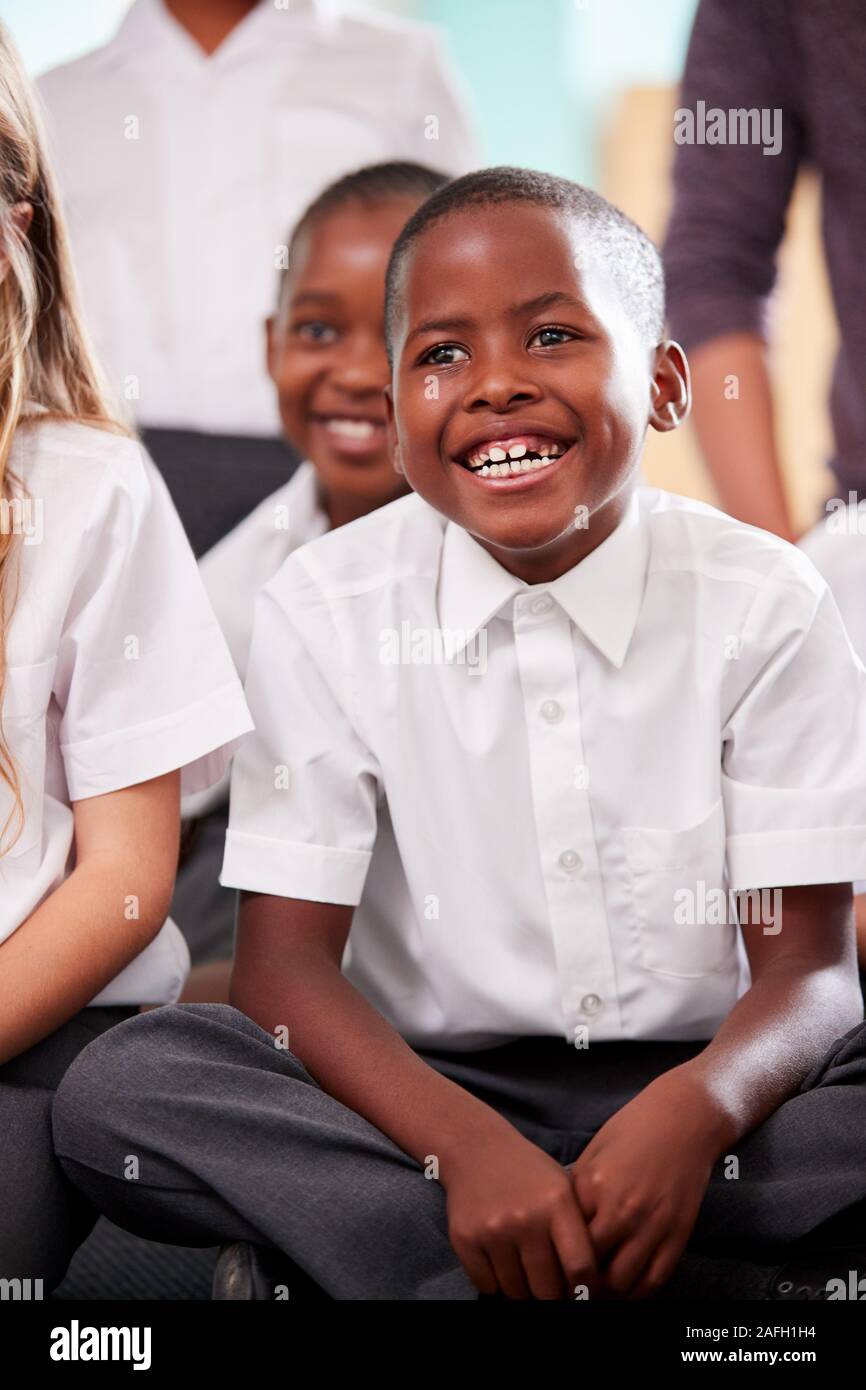 Group Of Elementary School Pupils Wearing Uniform Sitting On Floor Listening To Teacher Stock Photo