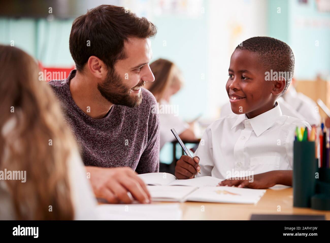 Elementary School Teacher Giving Male Pupil Wearing Uniform One To One Support In Classroom Stock Photo