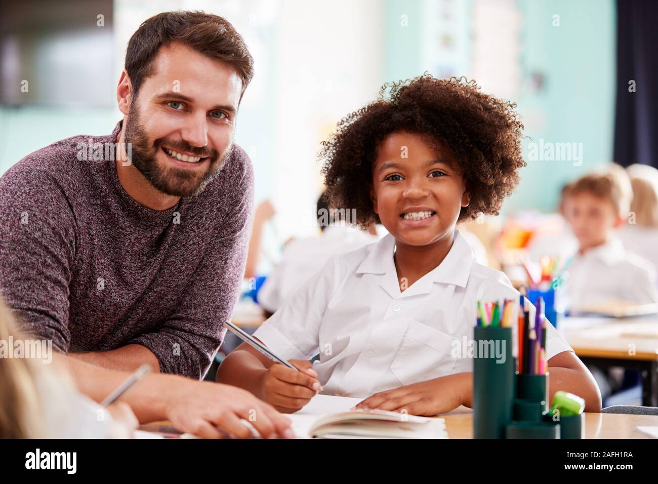 Portrait Of Male Elementary School Teacher Giving Female Pupil Wearing Uniform One To One Support Stock Photo