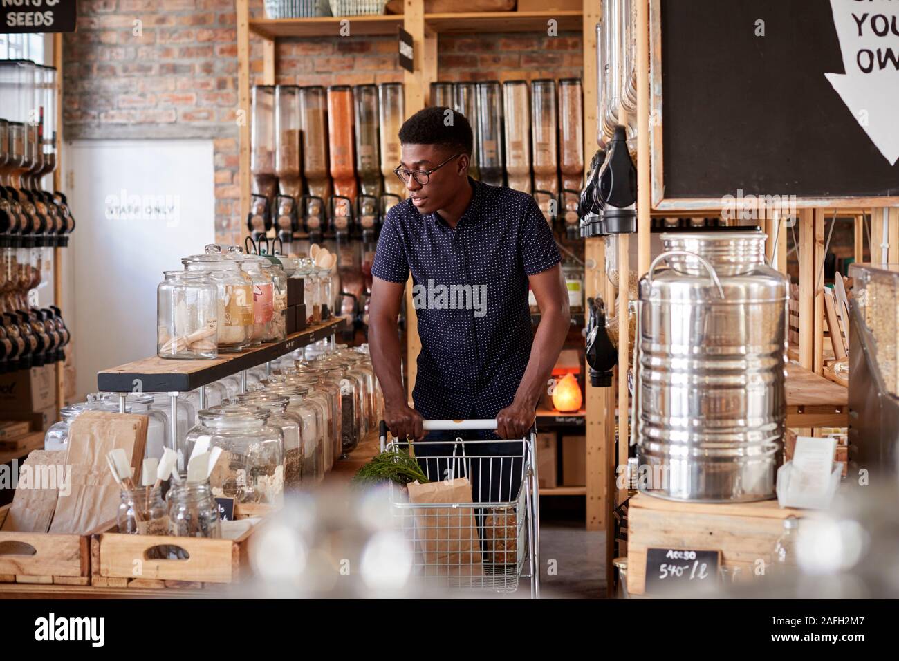 Man Pushing Shopping Trolley Through Dried Goods Section Of Sustainable Plastic Free Grocery Store Stock Photo