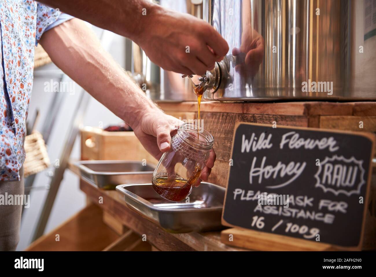 Man Filling Container With Wild Honey In Sustainable Plastic Free Grocery Store Stock Photo