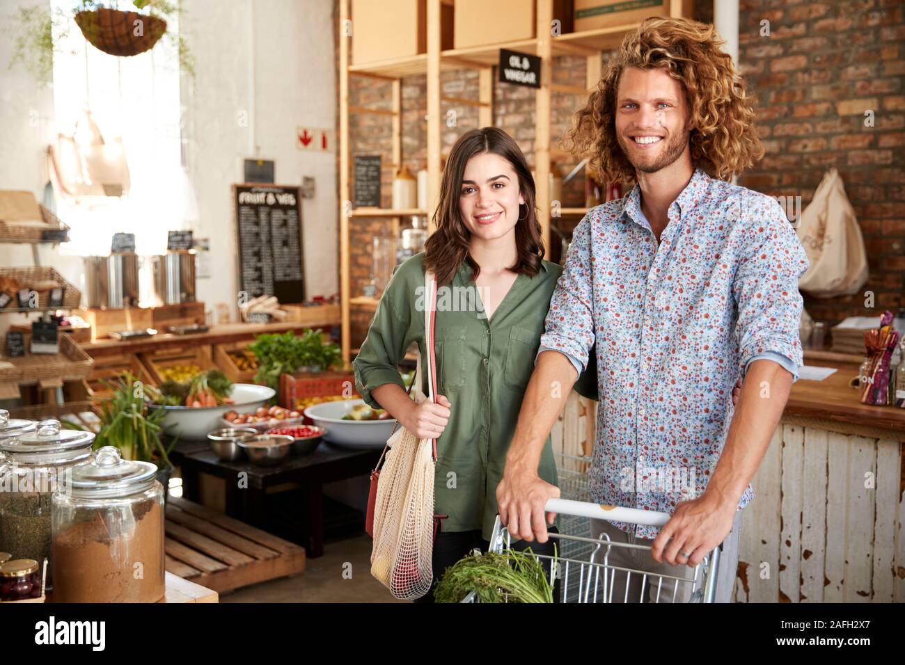 Portrait Of Couple With Trolley Buying Fresh Fruit And Vegetables In Plastic Free Grocery Store Stock Photo