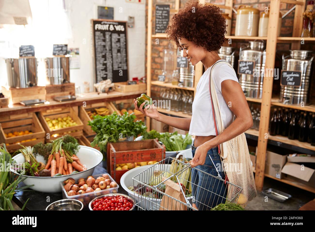 Woman Buying Fresh Fruit And Vegetables In Sustainable Plastic Free Grocery Store Stock Photo
