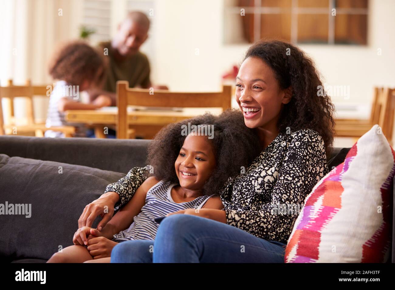 Mother And Daughter Sitting On Sofa At Home Watching Movie On TV Together Stock Photo